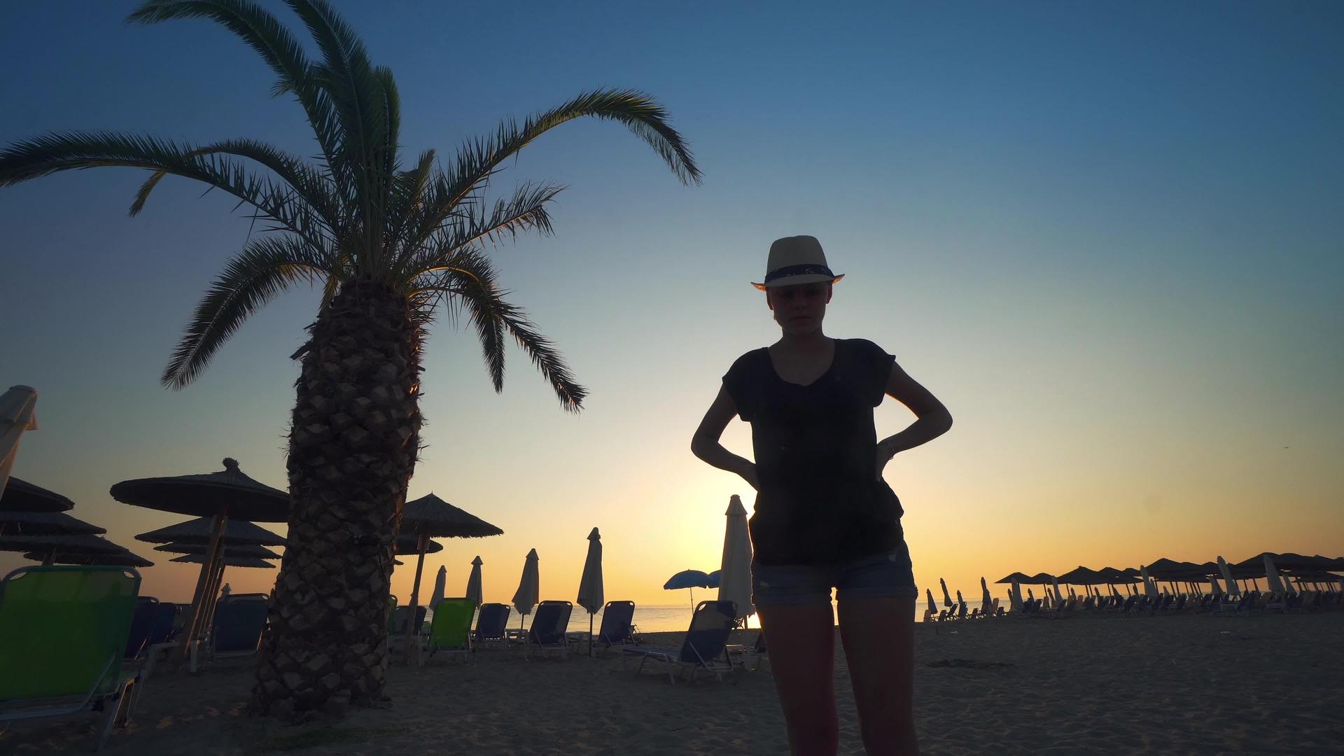 快乐美丽的年轻女子戴着草帽在夏天日落时站在双影观察视频的预览图