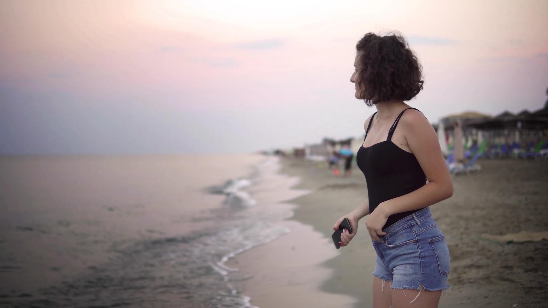 日落时无忧无虑的女人在沙滩上跳舞背景是棕榈树假期视频的预览图