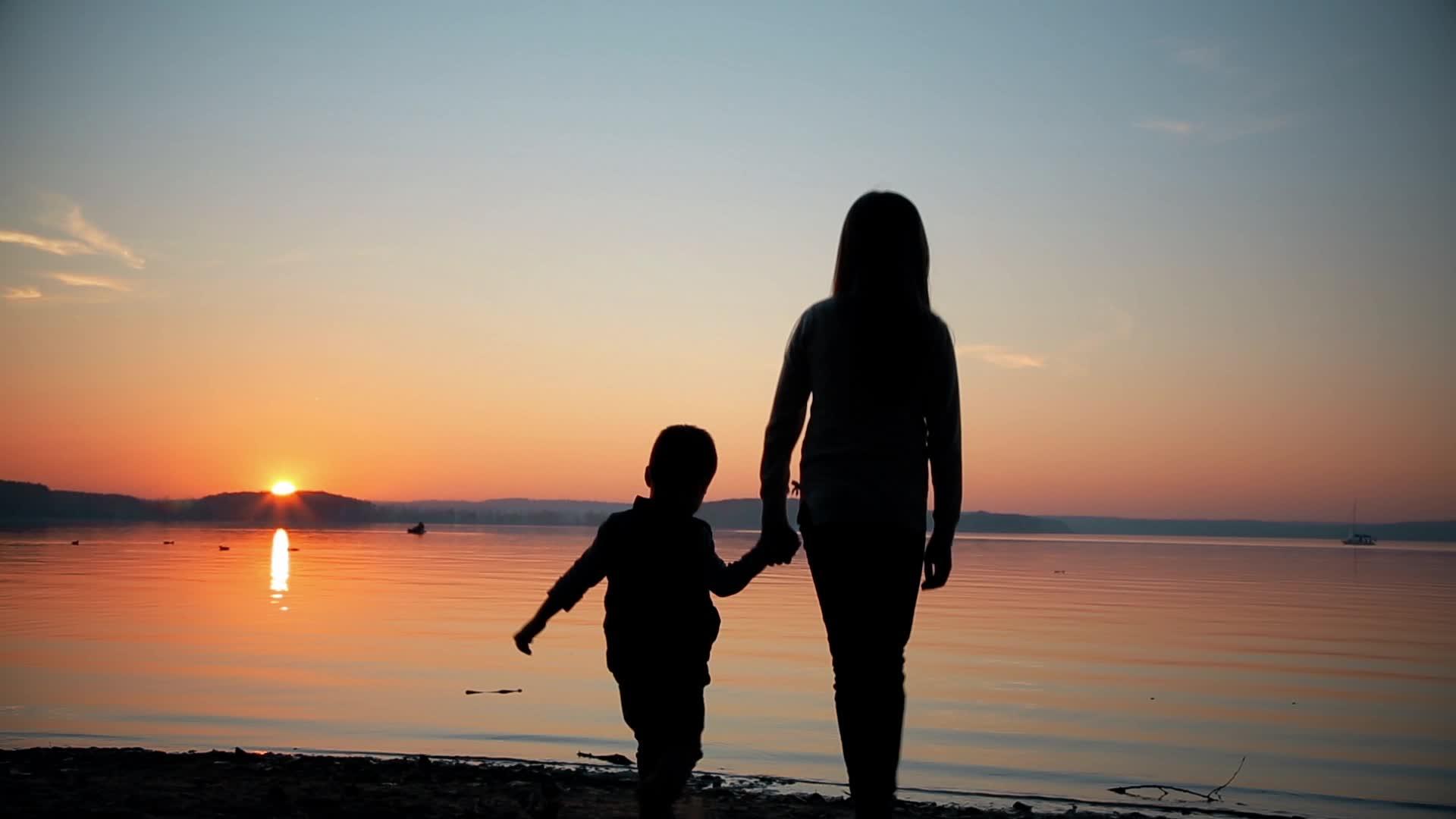 日落时女孩握着男孩的手向岸边走去视频的预览图