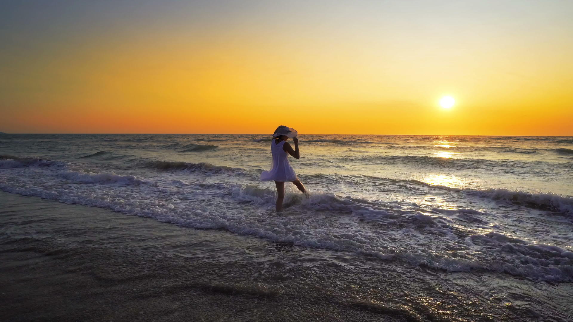 在海滩日落时戴着帽子的女人被海浪喷洒视频的预览图