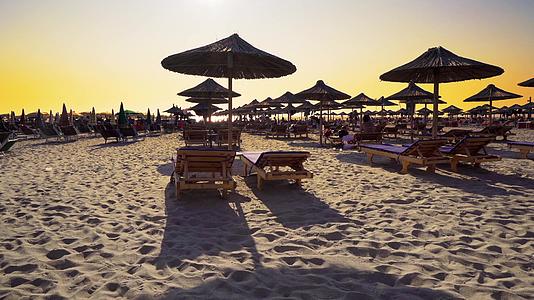 日落时海滩上的沙滩椅上挂着雨伞视频的预览图
