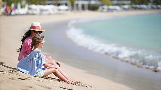 一家人坐在海滩上放松享受白色海滩的海景和笑声视频的预览图