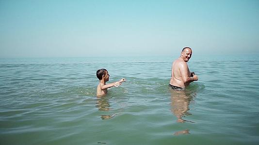 幸福的家庭父亲和儿子在海里游泳和喷水时玩得很开心视频的预览图