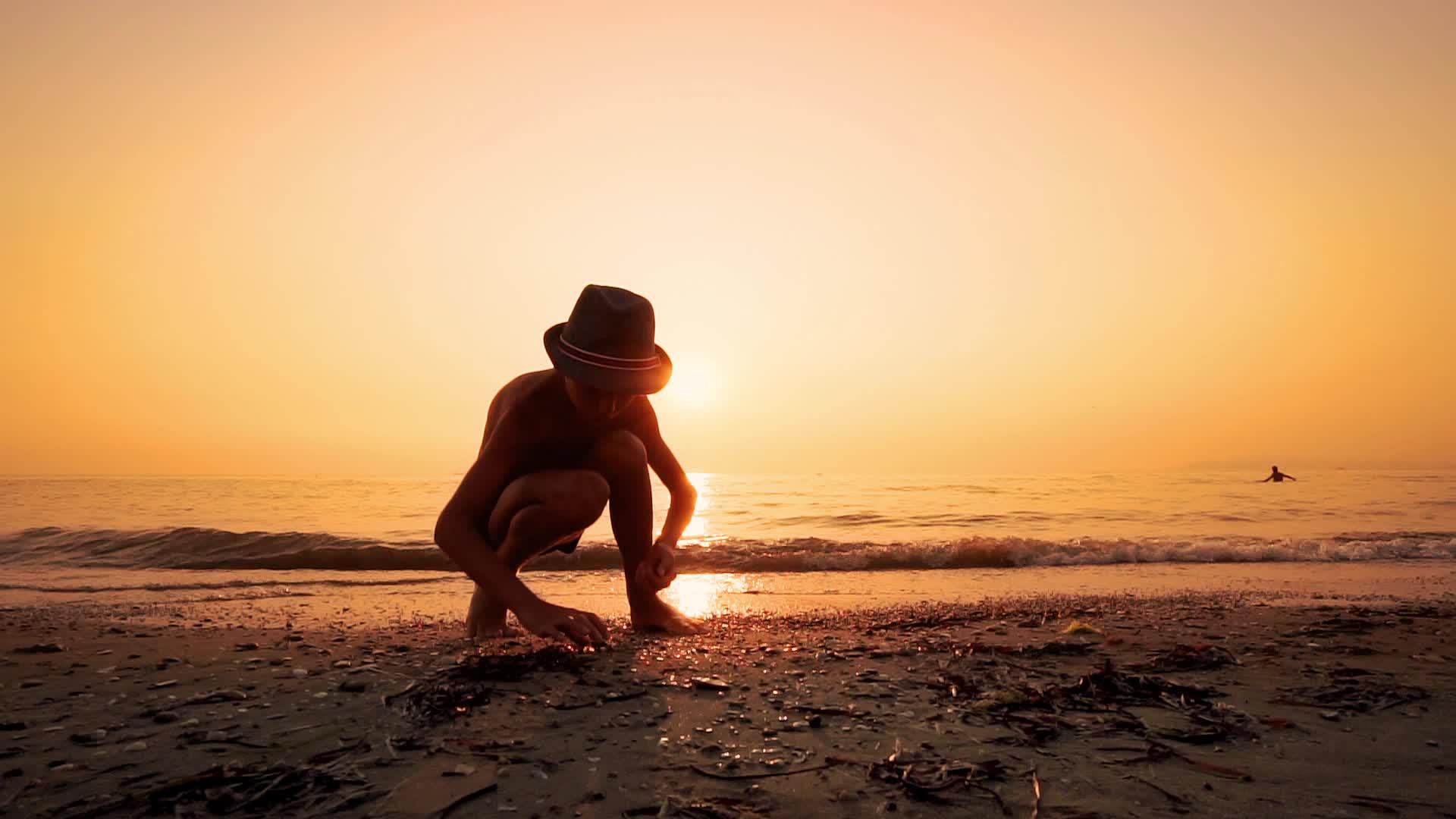 戴着帽子的男孩在海滩上寻找一块平石把它们看起来像跳石头视频的预览图