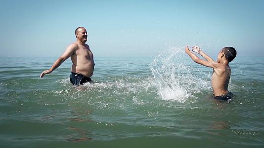 快乐的父子在海里玩耍——活跃的人们在海滩上跳舞和度假视频的预览图