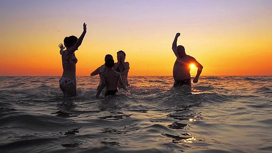 日落时一群家人和朋友游到海里潮湿地喷水慢慢地拍电影视频的预览图
