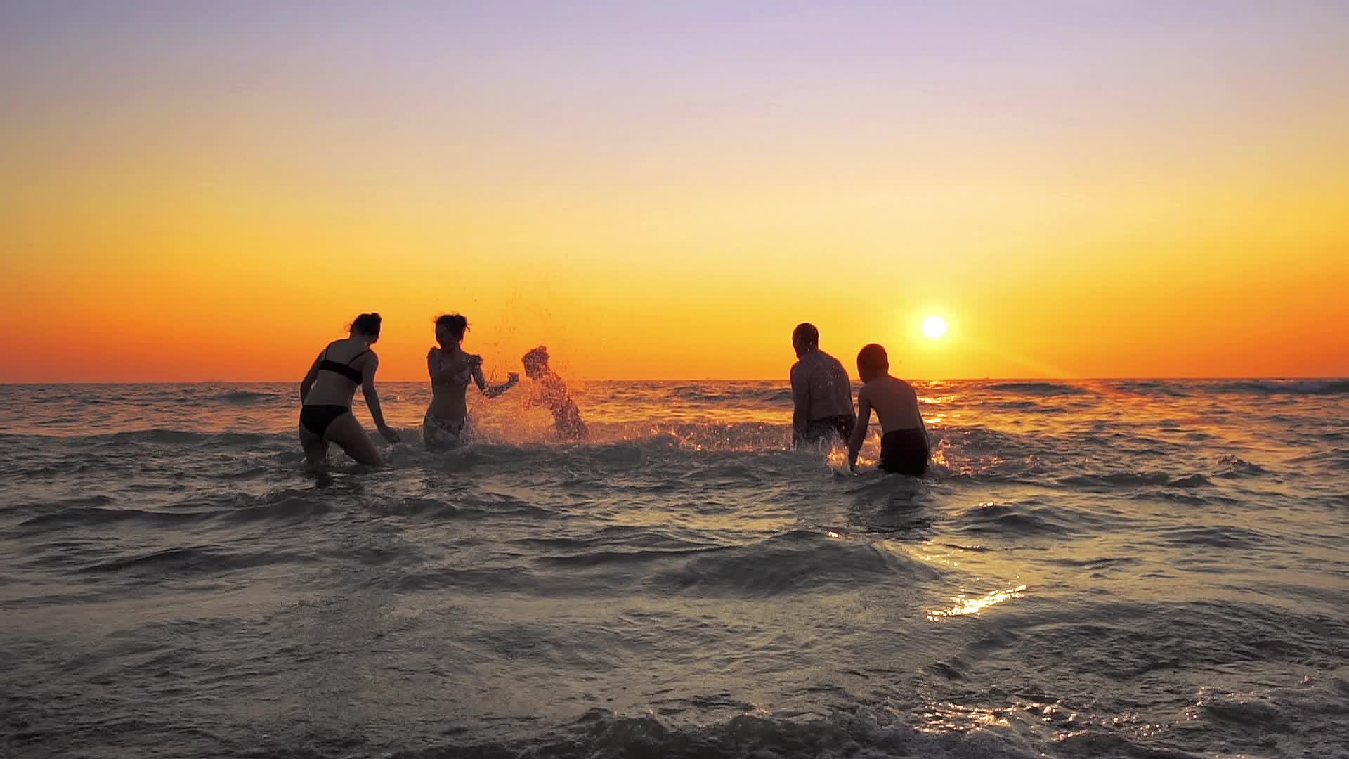 一群快乐的人在日落时在海滩上玩耍和喷水美丽而快乐视频的预览图