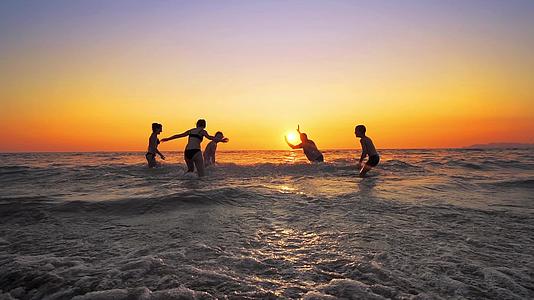 一群快乐的人在日落时在海滩上玩耍和喷水美丽而快乐视频的预览图
