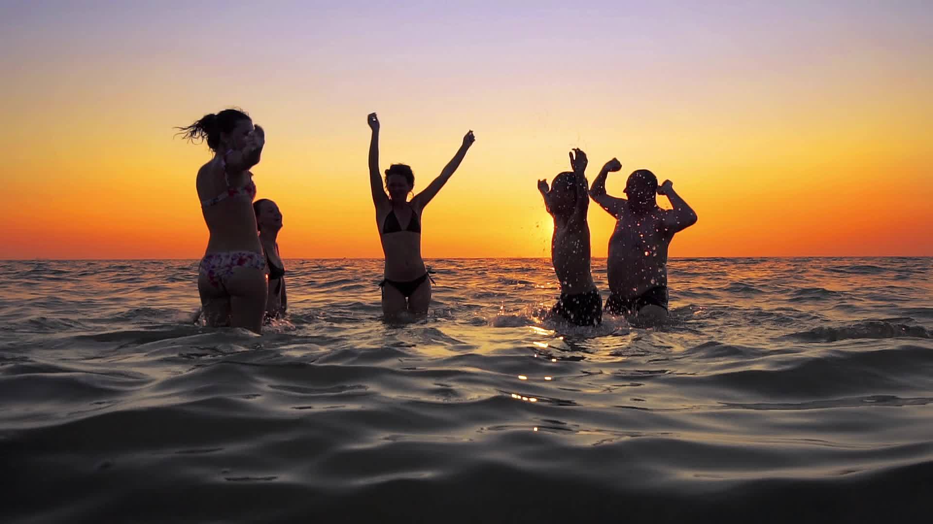 人们在海滩上日落时跳舞和喷洒青年欢乐派对视频的预览图