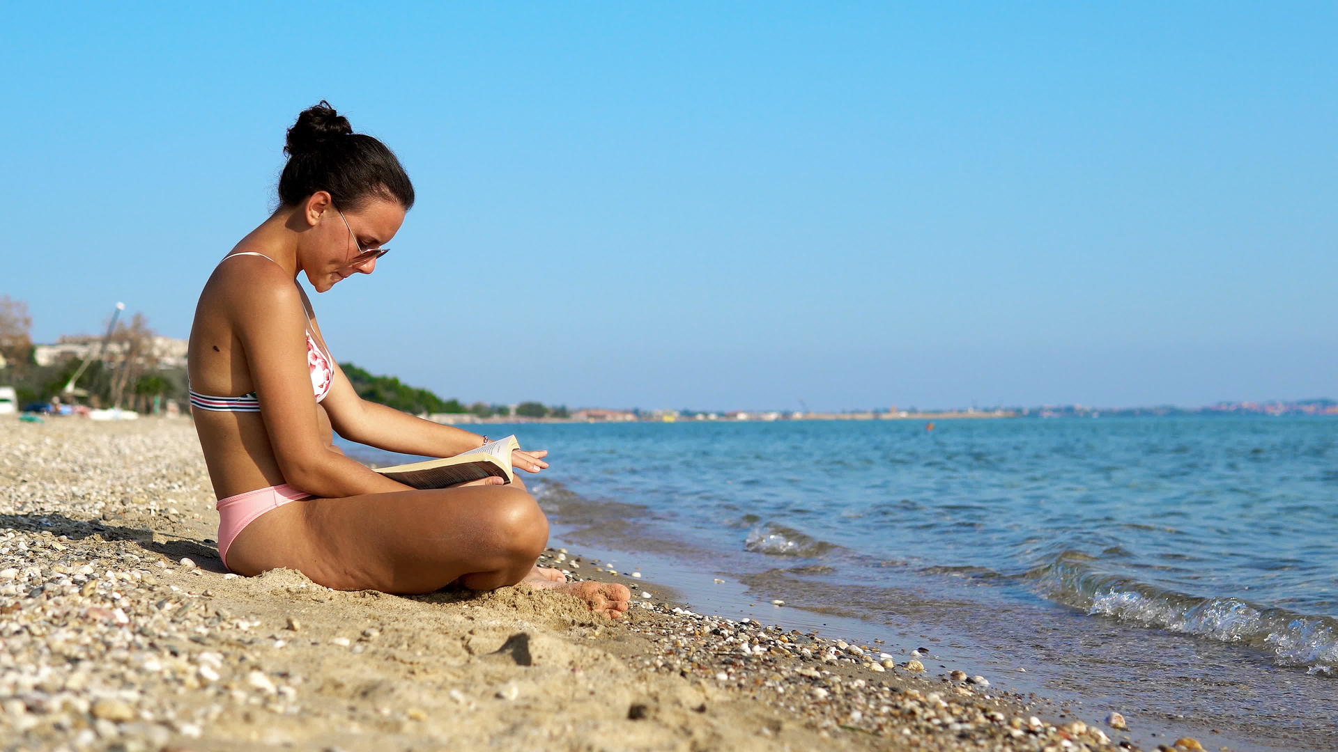 年轻女性在海滩上享受假期读一本书视频的预览图