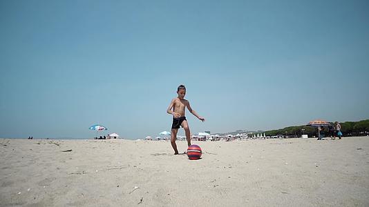 海滩上的小男孩玩足球、足球和慢动作视频的预览图