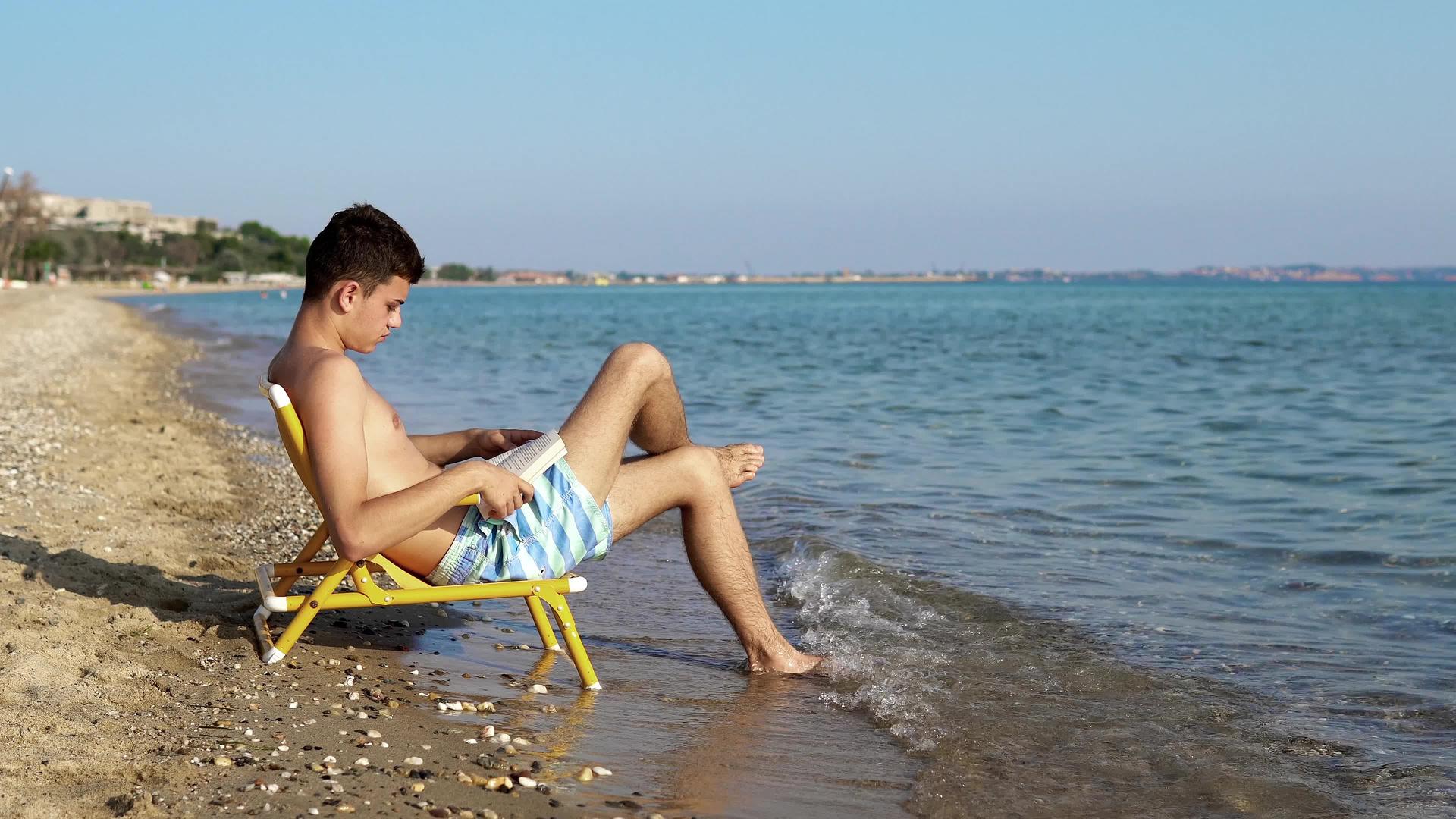 年轻人在海滩上背着波浪读了一本书视频的预览图