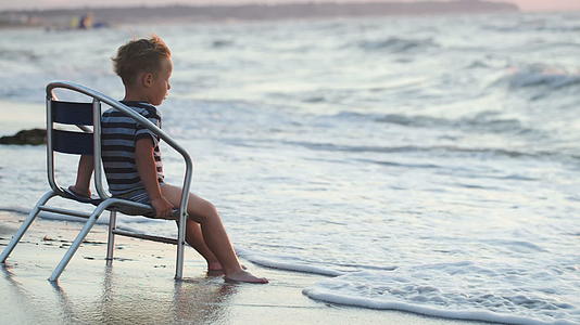 男孩坐在椅子上在海滩上洗脚视频的预览图