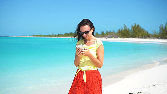 年轻女性在热带海滩度假期间使用移动智能手机视频的预览图
