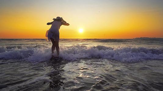 这位戴着帽子的年轻女士站在沙滩的水中仰望天空视频的预览图