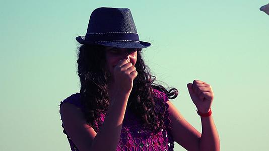 可爱的女孩戴着帽子在阳光明媚的海滩上跳舞视频的预览图