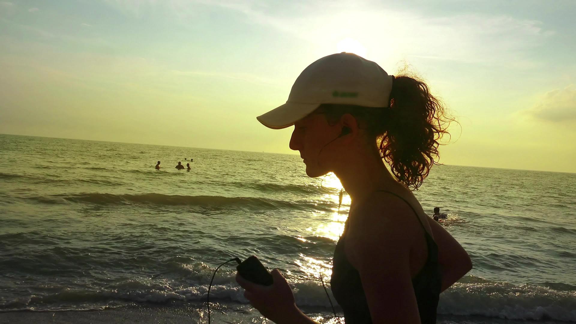 夏天海滩日落时配备马尾和耳机训练的跑步女孩慢跑视频的预览图