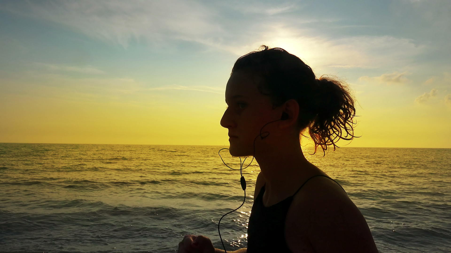 夏天海滩日落时配备马尾和耳机训练的跑步女孩慢跑视频的预览图