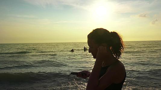 穿着马尾辫和耳机的漂亮女孩在夏天的海滩日落时放松和慢跑视频的预览图