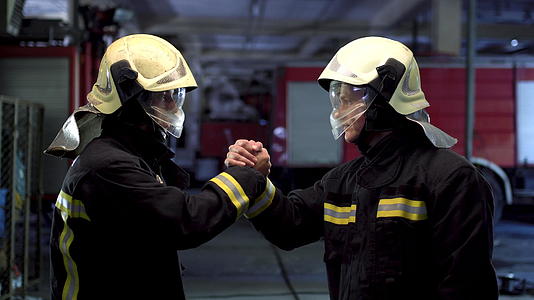 两名穿着制服和防护头盔的消防队员在背景中握手视频的预览图