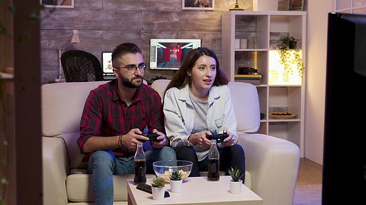 一对快乐的年轻夫妇坐在沙发上玩电子游戏视频的预览图