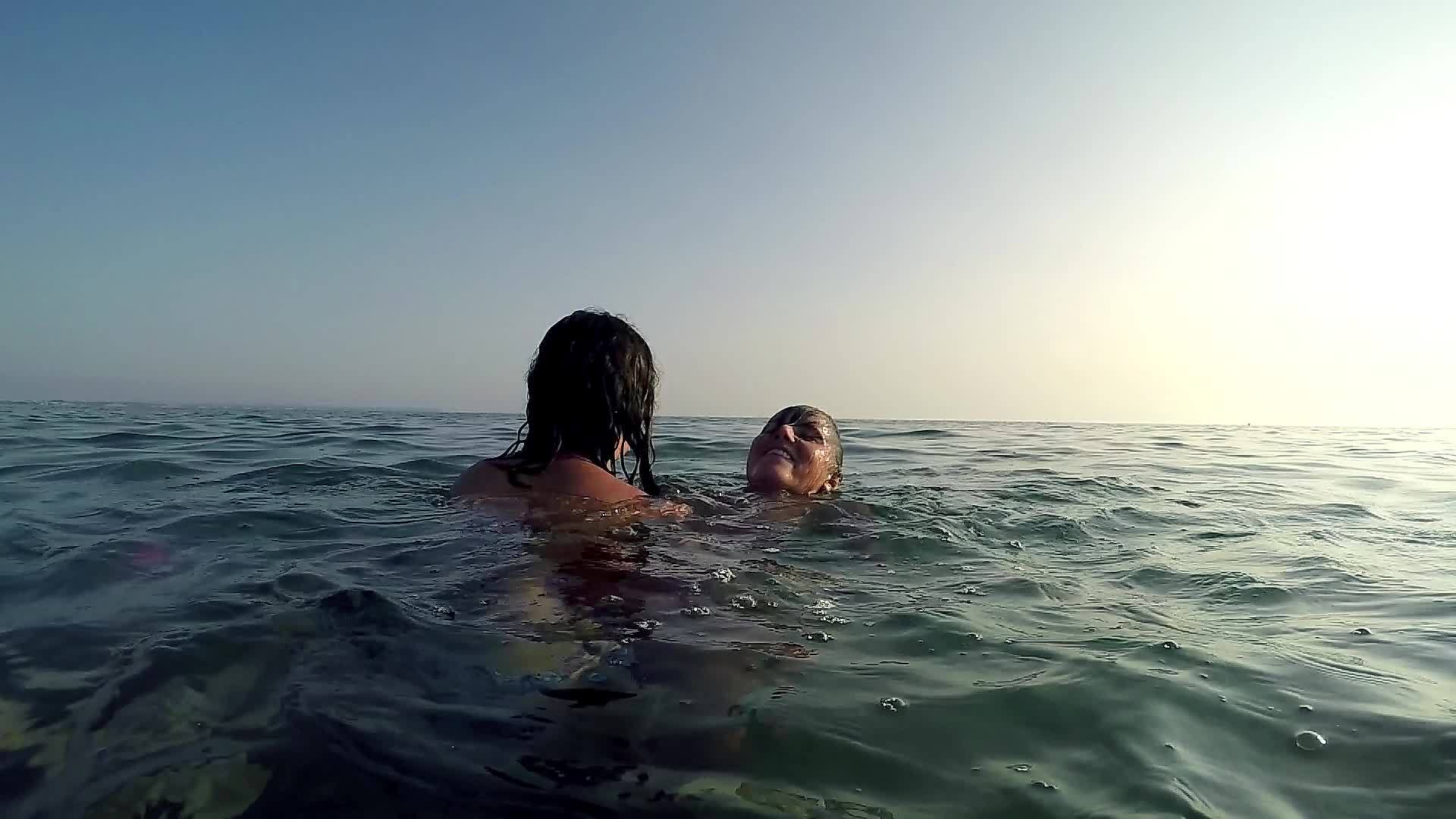 日落时两个快乐的女孩在海水表面玩溺水游戏视频的预览图