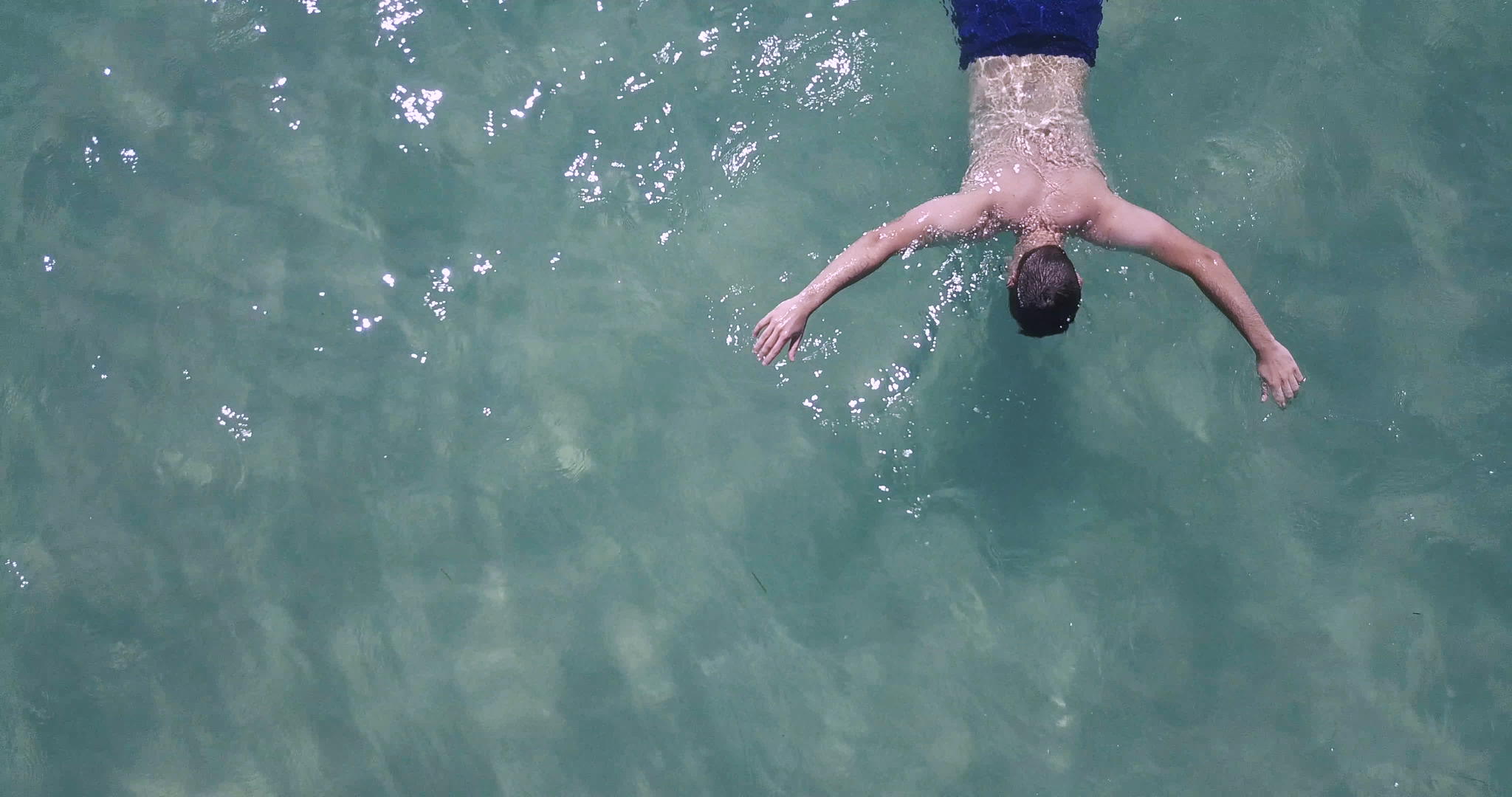 空中无人驾驶飞机射杀海中溺水的男子绿色的石头清澈的海水视频的预览图