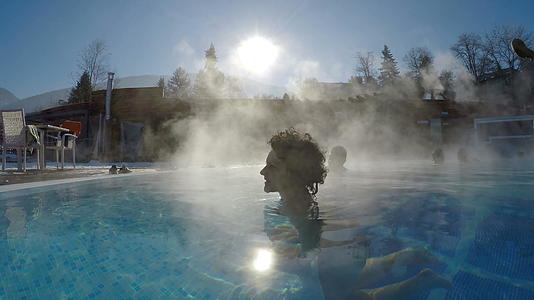 面对太阳你可以看到在室外热温泉游泳池里放松的美丽美女视频的预览图