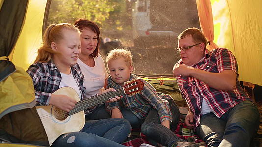旅游家庭在森林徒步旅行的露营帐篷里用吉他唱歌视频的预览图