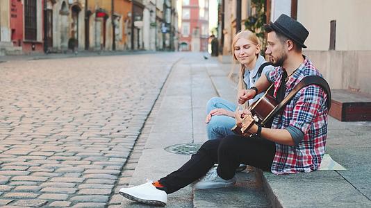 男人和女人坐在人行道上弹吉他和休息视频的预览图
