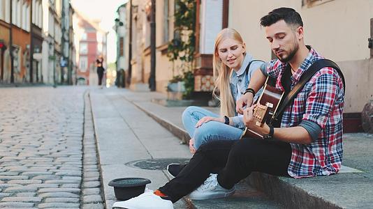 年轻的街头歌手坐在人行道上弹吉他和唱歌视频的预览图