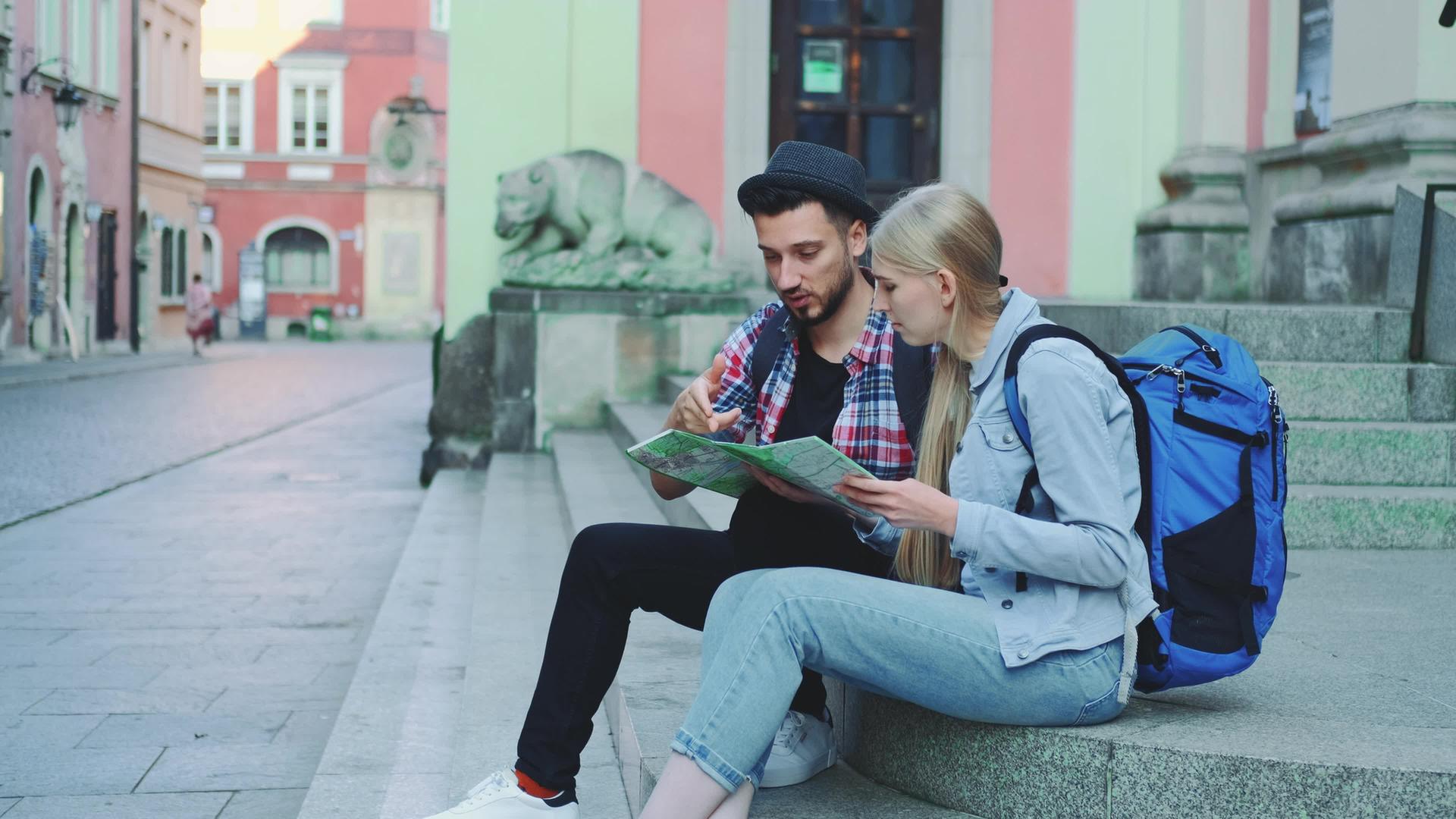 快乐的旅行情侣坐在街上的楼梯上检查城市地图讨论和讨论视频的预览图
