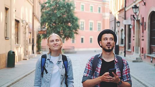 年轻的旅游夫妇走在街上用智能手机拍照视频的预览图