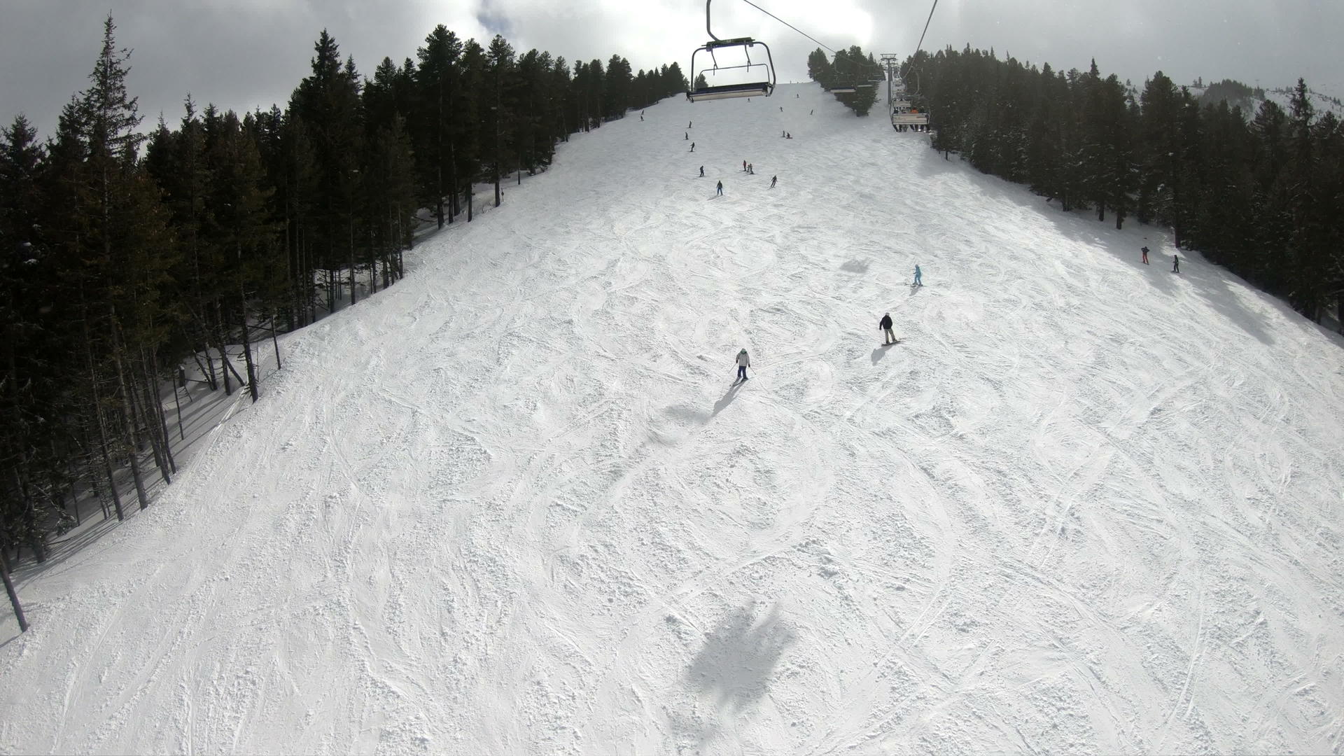 滑雪者和滑雪者在阳光明媚的天空下在滑雪胜地的山坡上下坡视频的预览图