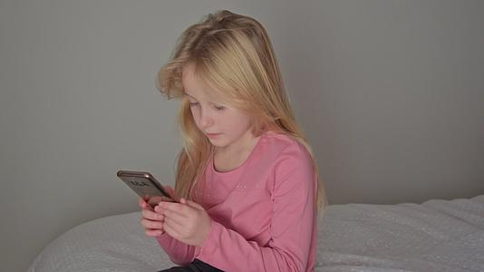 穿着粉红色小女孩的小女孩在家里的轻便卧室里打电话视频的预览图