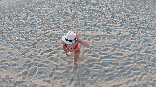 白色帽子的年轻女性在阳光明媚的白天在海滩上散步视频的预览图