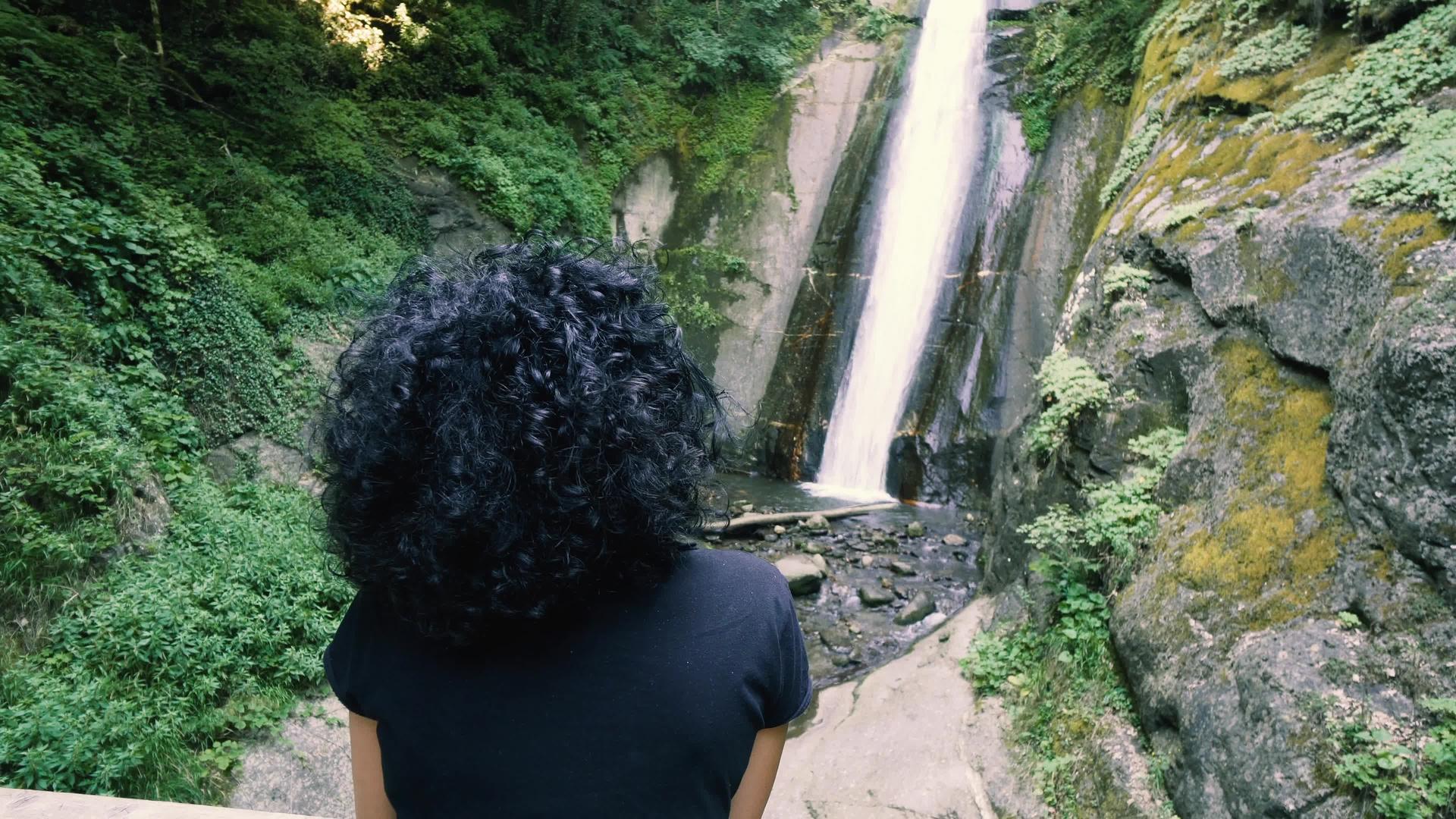 穿着卷发的女孩享受森林瀑布的风景视频的预览图