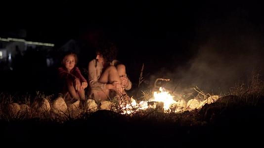 母亲和女儿坐在一个明亮的营火周围视频的预览图