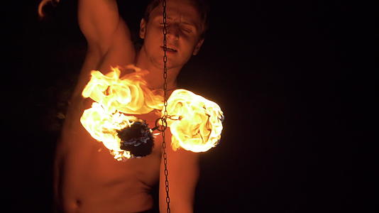 肌肉发达的男人在火表演链上旋转两个火球视频的预览图