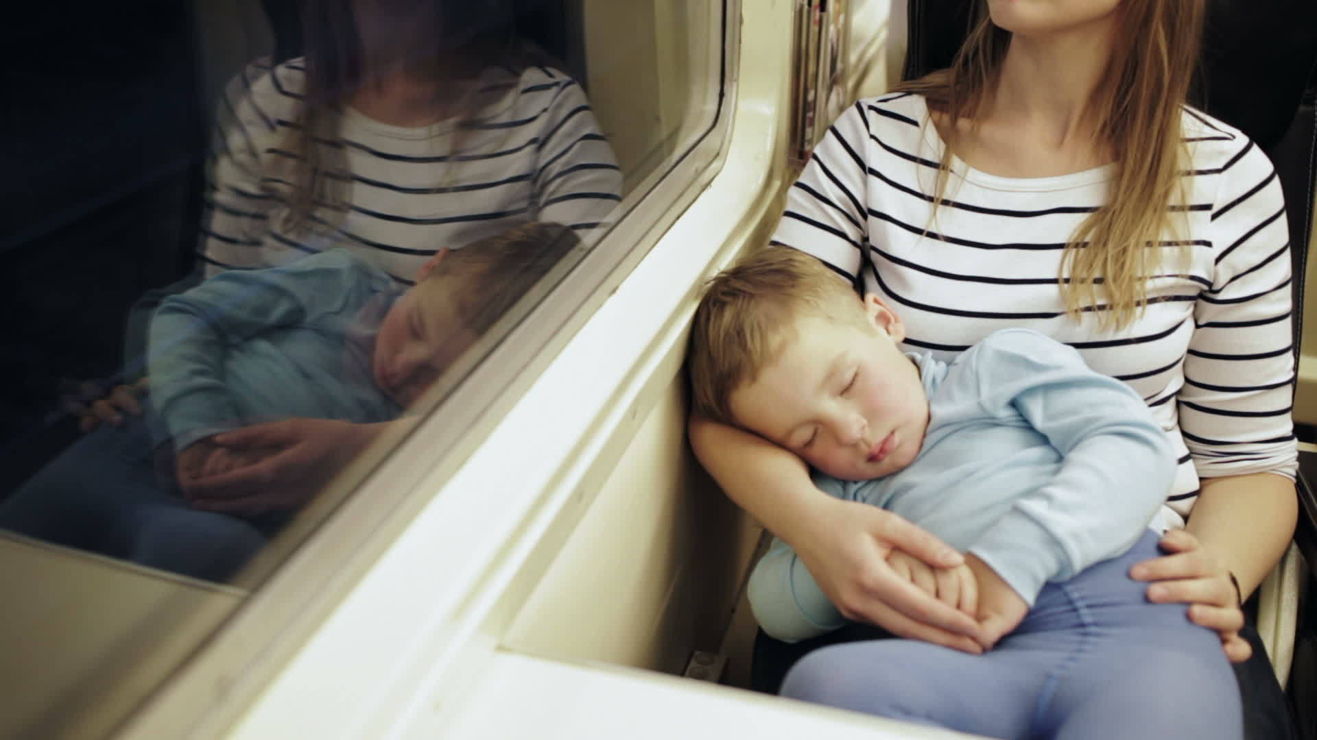 一个疲惫的女人在火车上睡着的儿子在她的腿上视频的预览图