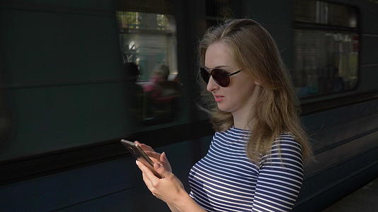 年轻女孩穿着条纹衬衫和长发太阳镜在地铁站停留和使用视频的预览图