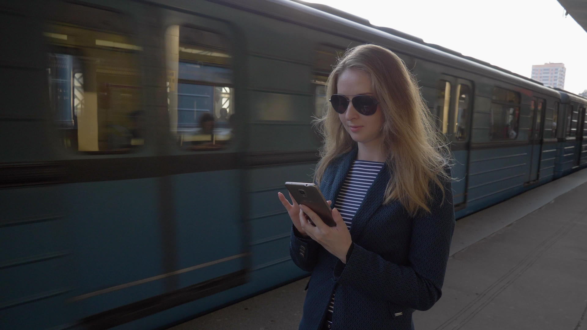 住在地铁站的年轻女孩穿着蓝色夹克和长发太阳镜使用它们视频的预览图