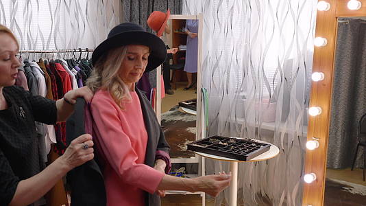 灰色头发的高级女性在陈列室工作室试穿新外套服装设计师视频的预览图