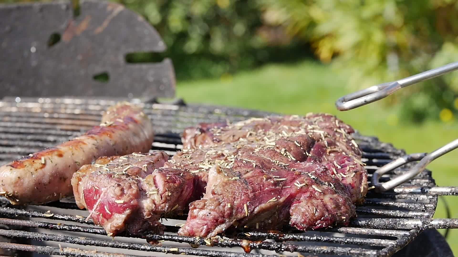在烧烤和绿草的背景下牛排和猪肉香肠视频的预览图