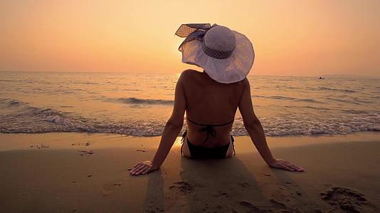 戴帽子的性感女性享受热带海滩的日落和海浪飞溅视频的预览图