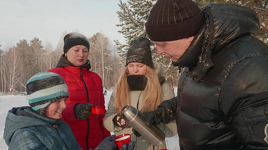 冬天在森林里散步的家庭父亲从温热的酒瓶里倒热茶喝热茶视频的预览图