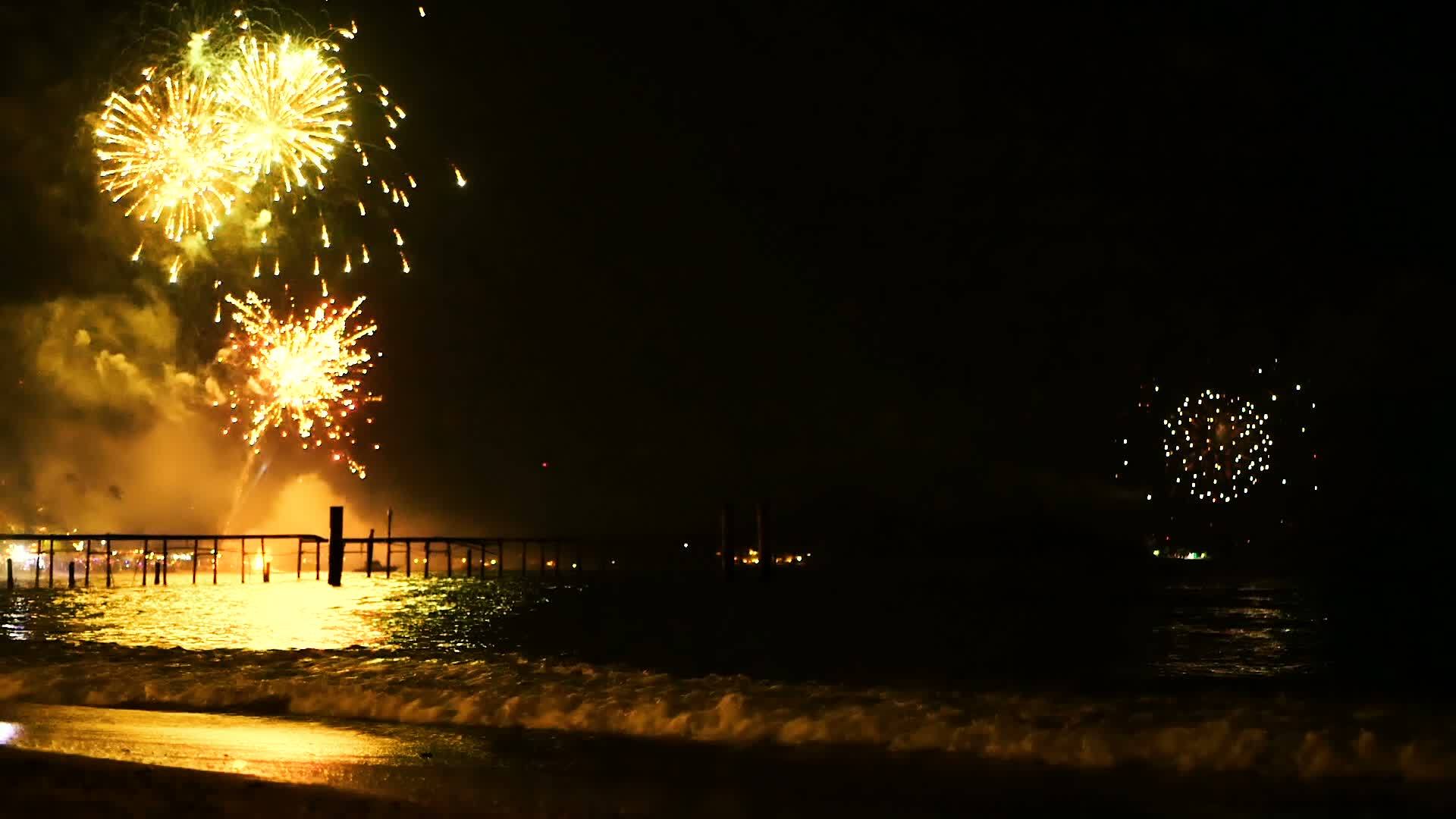 明亮的金色烟花在海面上空的夜空中爆炸视频的预览图