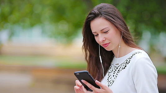 公园里年轻的白人妇女用她的智能手机在户外发送信息视频的预览图