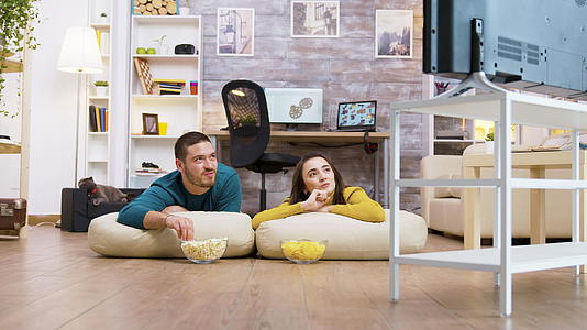一对夫妇坐在地板的枕头上看电视聊天视频的预览图