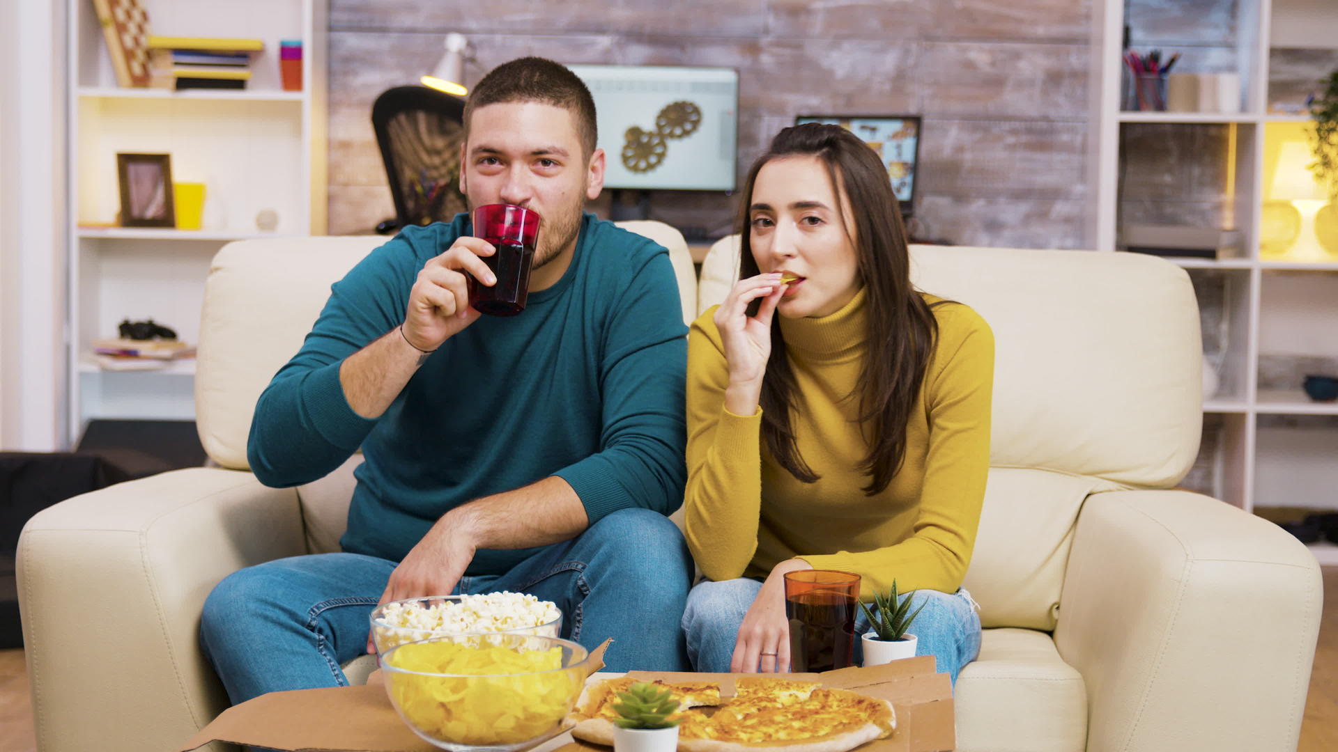 情侣们坐在沙发上笑着看电视吃披萨视频的预览图
